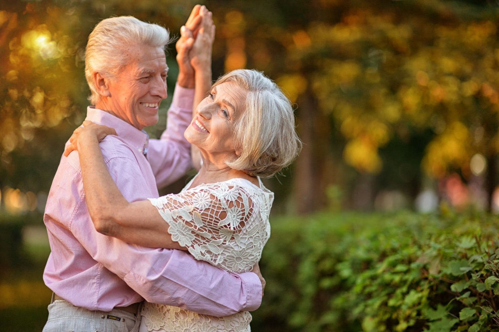 An older couple dancing together in a park in evening light