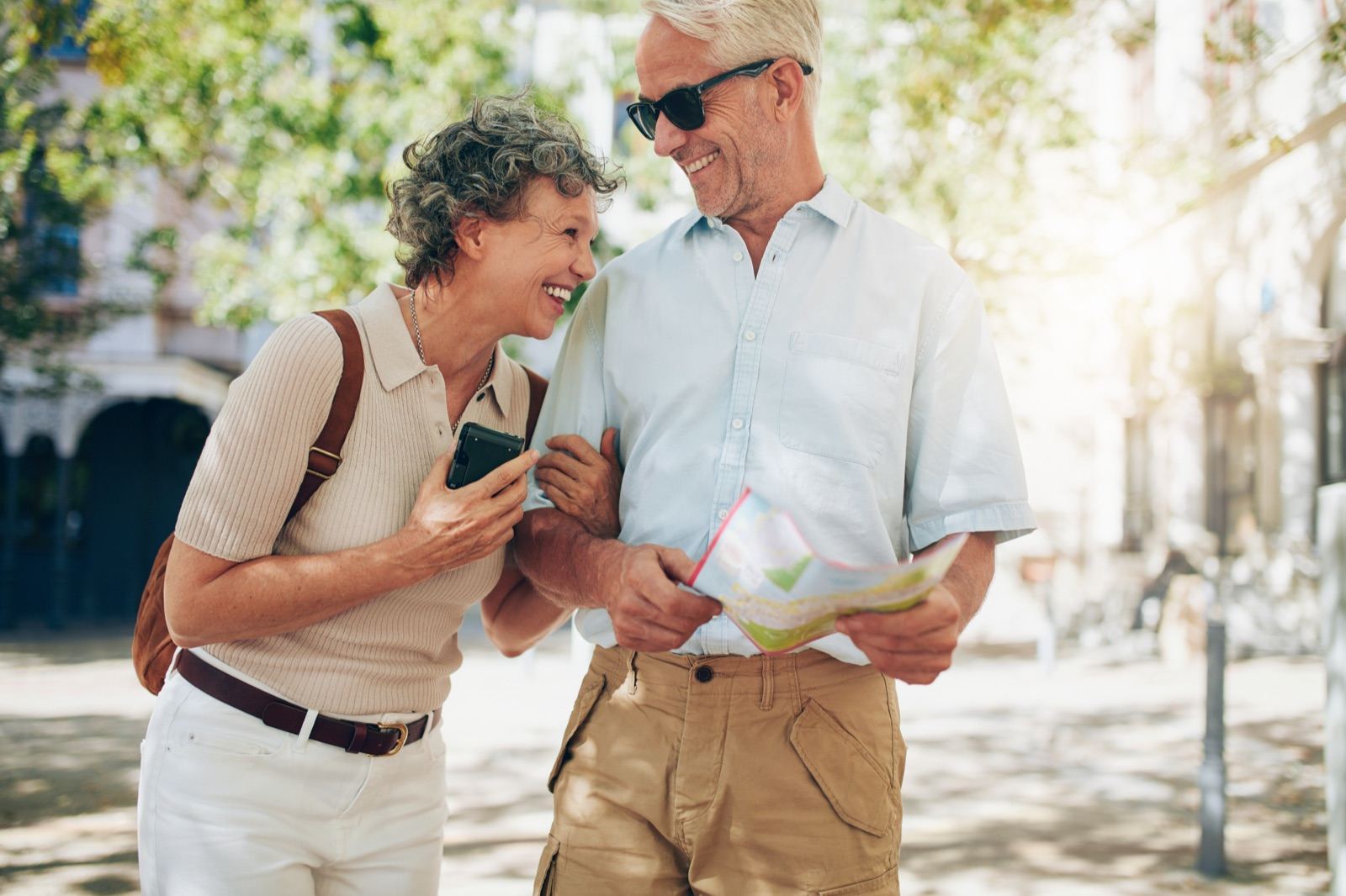 A couple walking together on a sunlit street, looking at a phone and a map